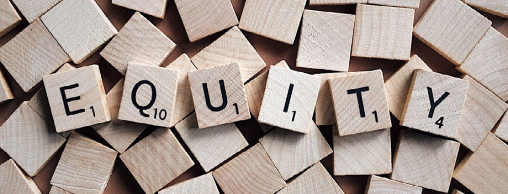 Wooden Scrabble tiles spell out the word EQUITY on top of a scattered pile of blank wooden tiles, symbolizing educational equity and the benefits it brings to students.