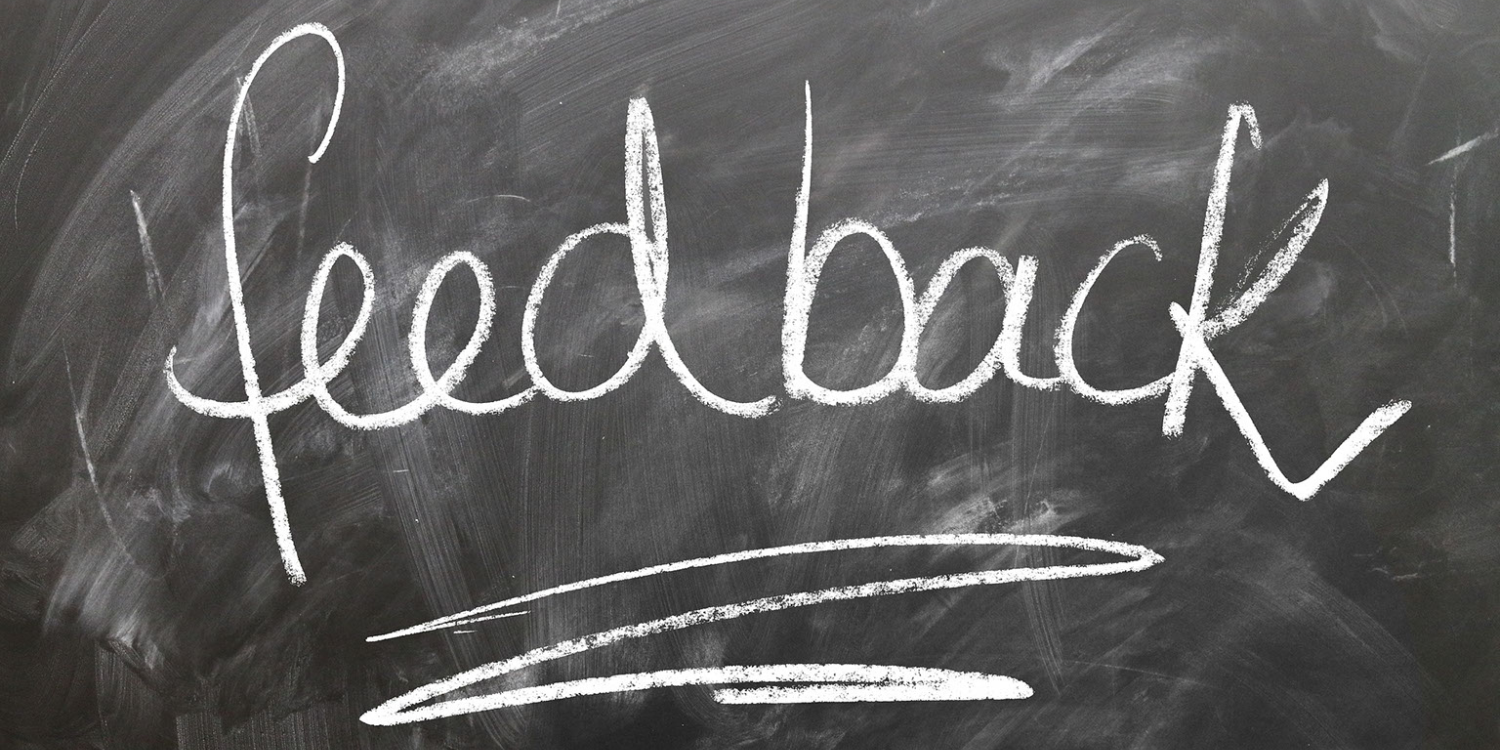 The word feedback is written in large, white chalk letters on a black chalkboard, with two curved lines drawn underneath for emphasis—highlighting its importance in fostering a positive learning culture.