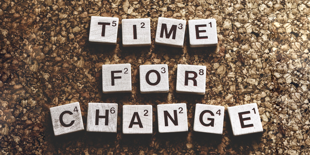Scrabble tiles arranged on a speckled brown surface spell out TIME FOR CHANGE, with each letter showing its game point value—a subtle nod to the urgent need to address school segregation and educational inequality.