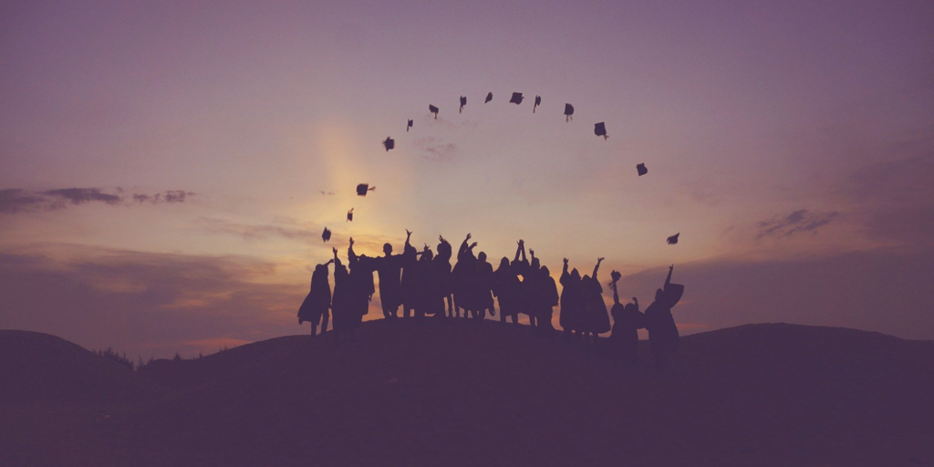 Silhouetted group of graduates in caps and gowns stand on a hill at sunset, joyfully tossing their caps into the air—a celebratory scene inspired by rising high school graduation rates in New England.
