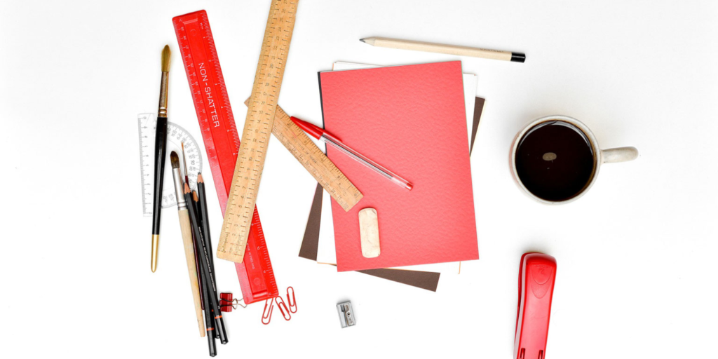 Assorted stationery, including rulers, pens, pencils, brushes, a stapler, a notebook, paperclips, and a cup of coffee—perfect tools for fostering community engagement—arranged on a white surface.