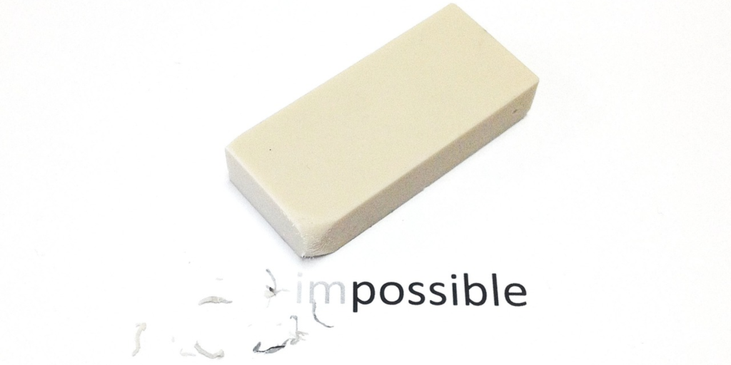 A white eraser, symbolizing possibility, partially erases the word impossible on white paper, revealing possible and transforming impossibility into opportunity.