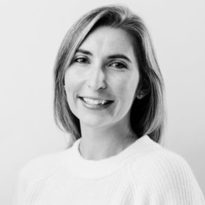 Black and white portrait of Paulina Murton, a woman with straight, shoulder-length hair, wearing a light-colored sweater and smiling gently at the camera against a plain background.