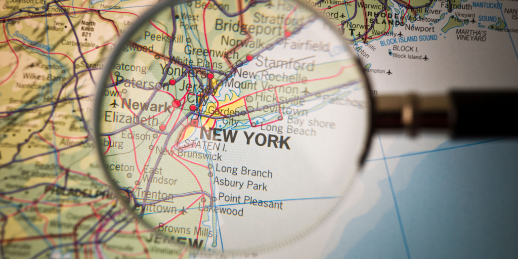 A close-up of a map focused on New York City and nearby areas, viewed through a magnifying glass, highlighting locations where social impact leaders make a difference—from Newark and Jersey City to Long Beach.