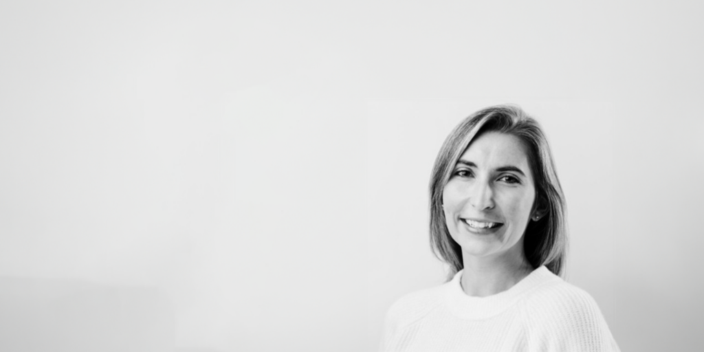 Executive Director Paulina Murton, with shoulder-length hair and a light-colored sweater, smiles at the camera. The black and white image features a plain, light background.
