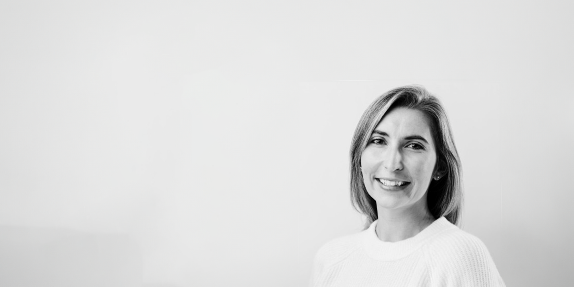 Executive Director Paulina Murton, with shoulder-length hair and a light-colored sweater, smiles at the camera. The black and white image features a plain, light background.