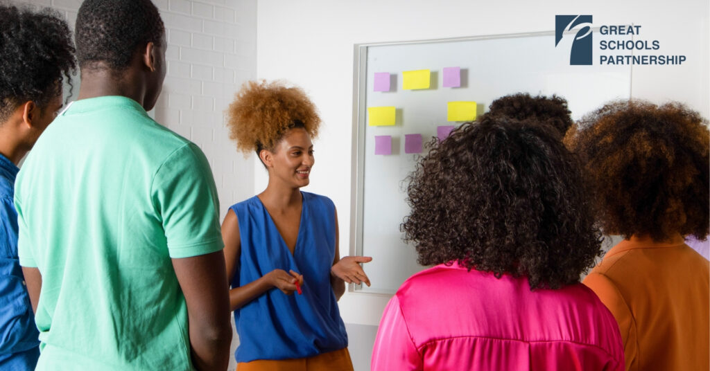 A women addresses a group of BIPOC adults, smiling and holding out her hands.