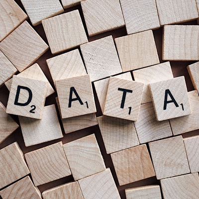 Scrabble tiles spelling the word DATA are arranged on top of a scattered pile of blank wooden tiles, highlighting the importance of data.