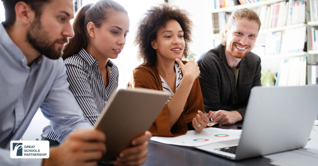Four people sit together at a table, looking at a laptop and tablet, discussing data charts and graphs. They appear engaged and collaborative. A “Great Schools Partnership” logo is visible in the bottom left corner.