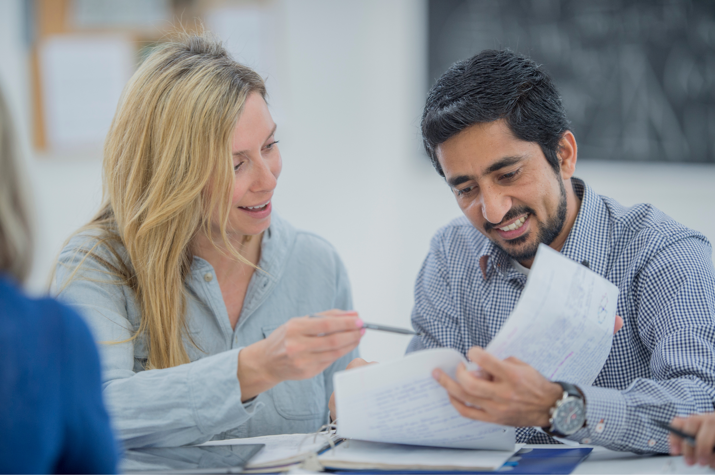 A woman and a man sit together at a table, smiling and reviewing notes or documents during their Discovery Sessions, with the woman pointing at the papers using a pen.